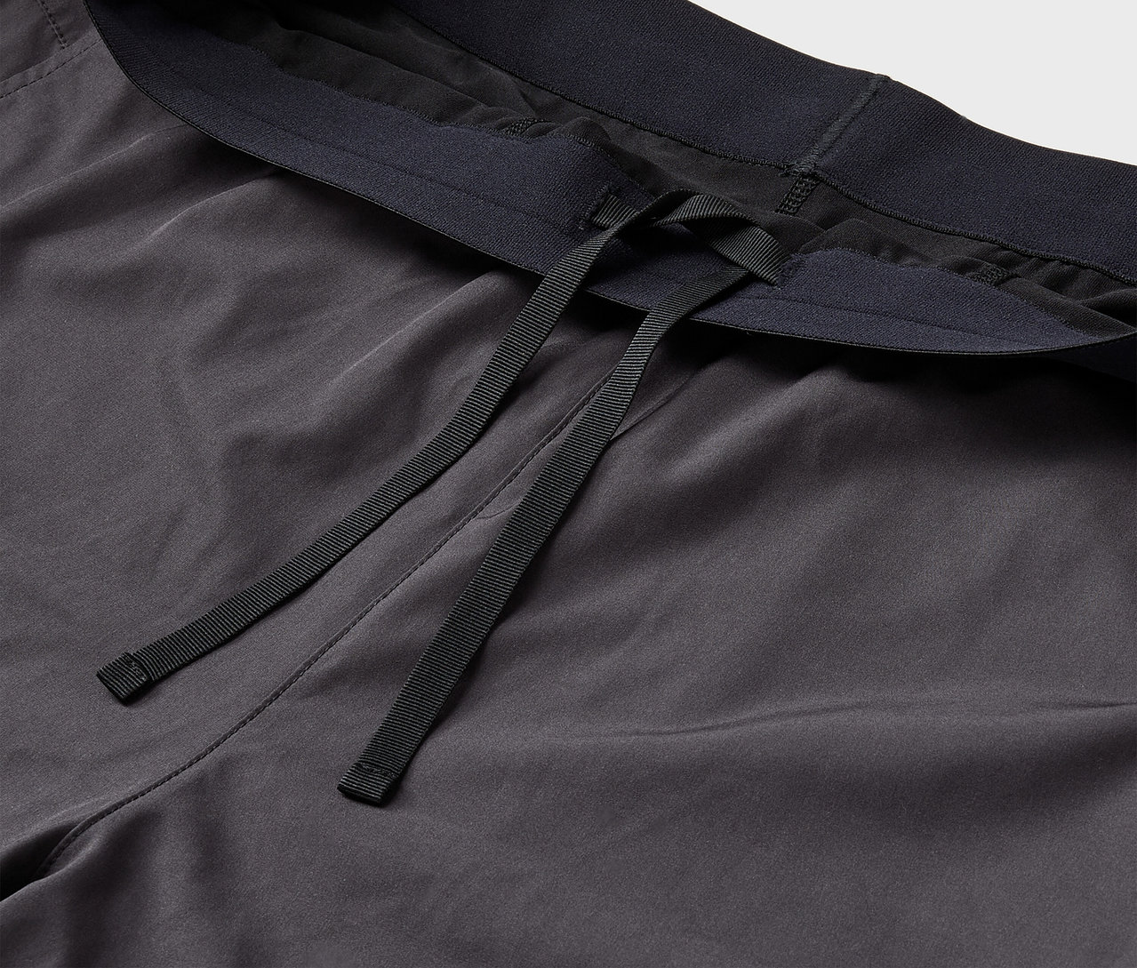 Detail sivých športových nohavíc s čiernou gumou v páse a šnúrkami.