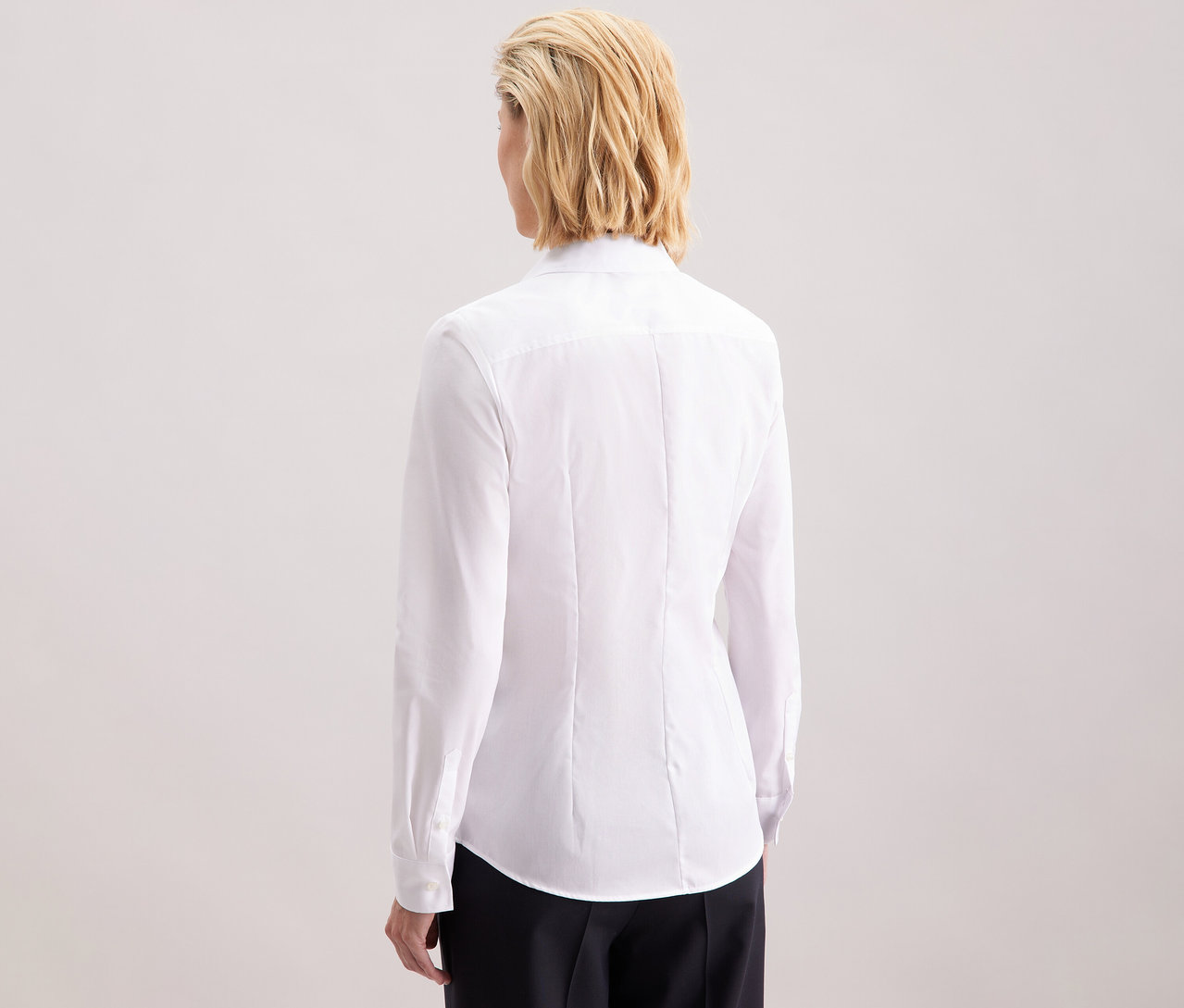 Pohľad zozadu na blondínku s vlasmi po plecia v bielej blúzke Seidensticker Slim Fit non iron.