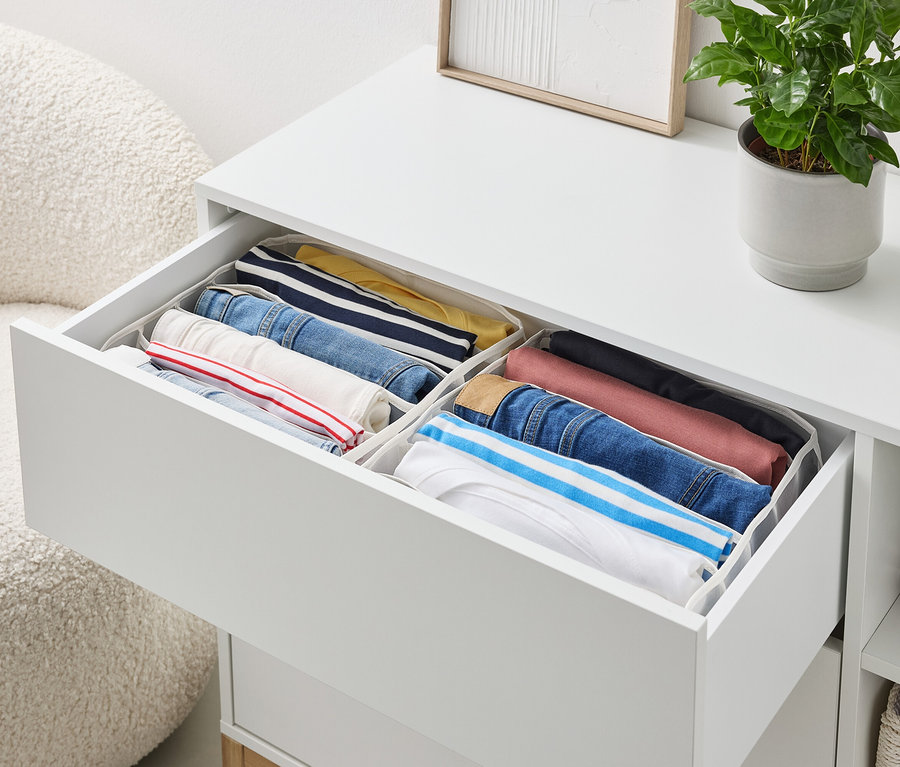 Otvorená zásuvka bielej komody obsahuje úhľadne poskladané oblečenie v organizéroch.