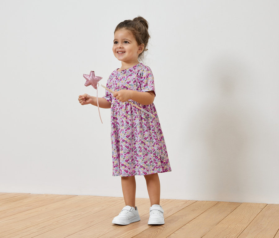 Usmievajúce sa dievčatko drží hviezdnu paličku a má na sebe kvetinové šaty a tenisky.