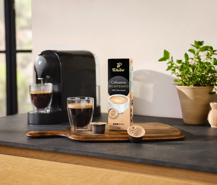 Kávovar naleje kávu do sklenice vedľa balenia kapsúl Cafissimo Decaffeinato.