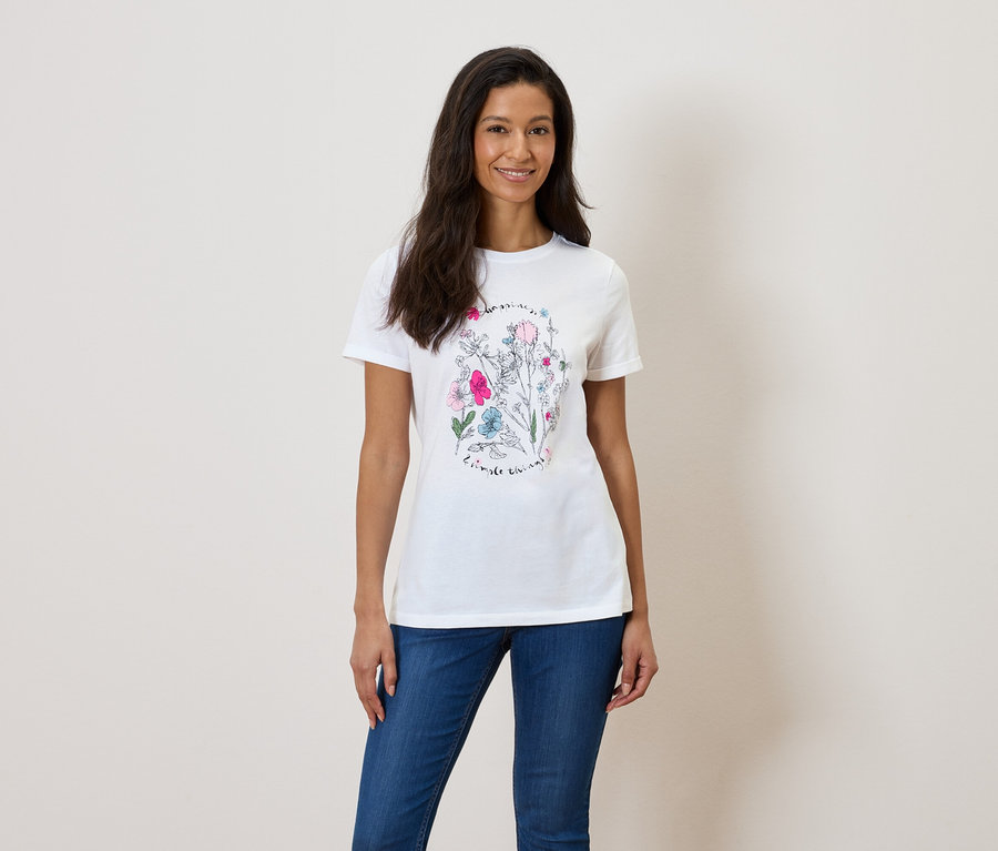 Žena má na sebe biele tričko s kvetinovou potlačou a modré džínsy.