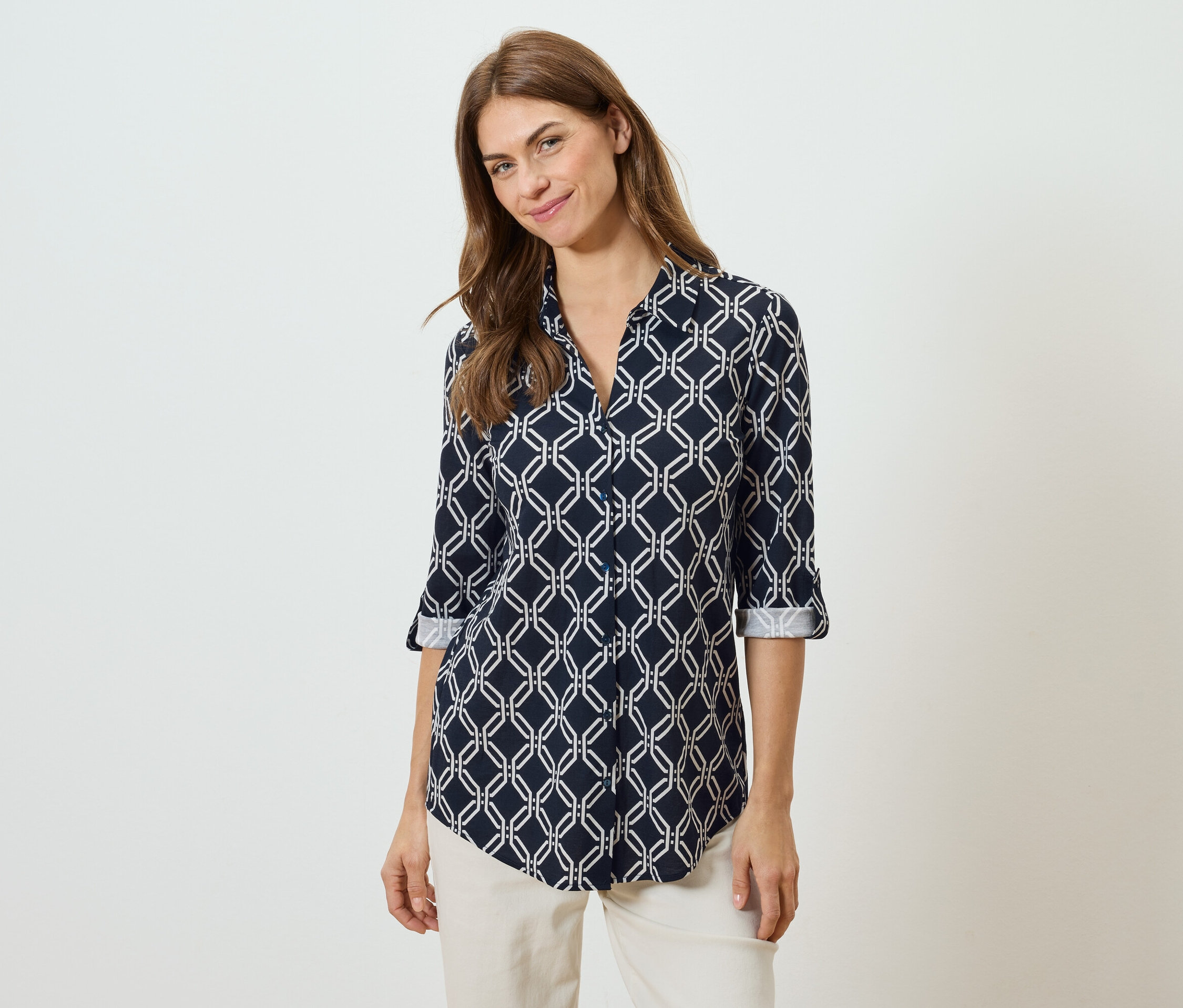 Žena má na sebe tmavomodrú blúzku s bielym geometrickým vzorom a béžové nohavice.