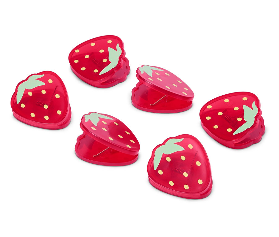 Šesť červených sponiek v tvare jahôd leží na bielom povrchu.