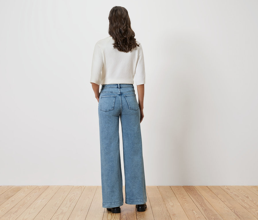 Žena stojí chrbtom ku kamere a má na sebe svetlú blúzku a široké džínsy.