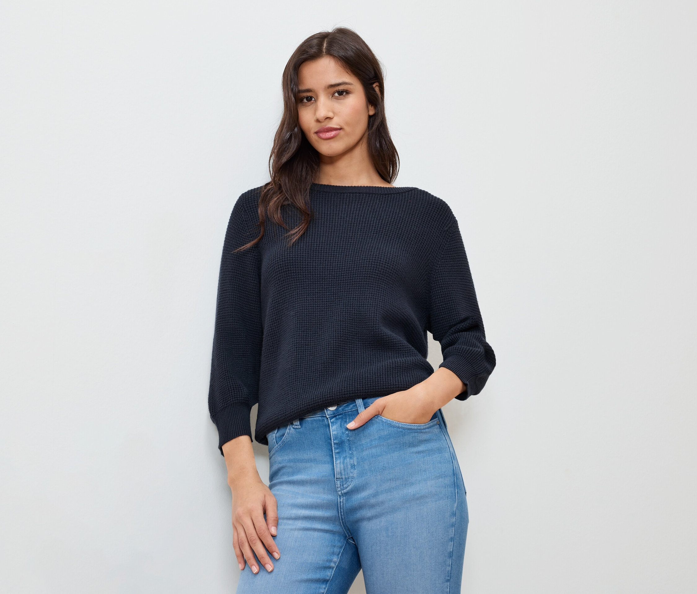 Žena s rukou vo vrecku nosí tmavomodrý jemný pletený sveter.