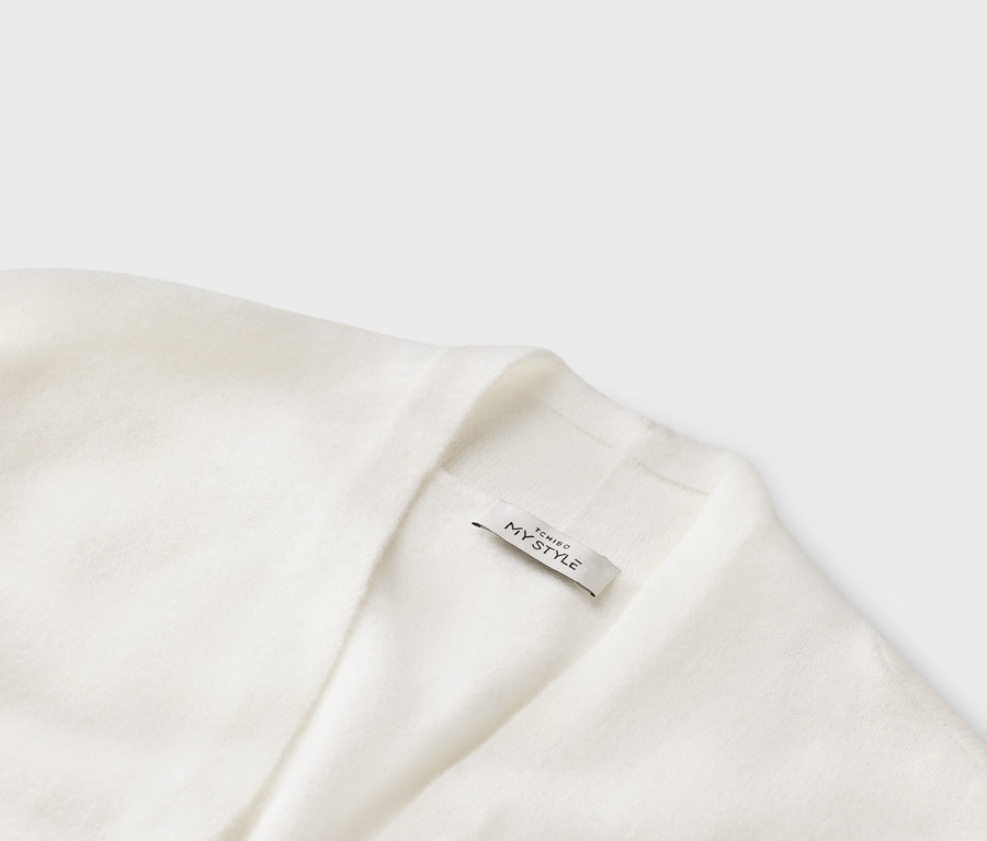 Detailný záber na biely pletený kardigán s etiketou s nápisom „TCHIBO MY STYLE“.