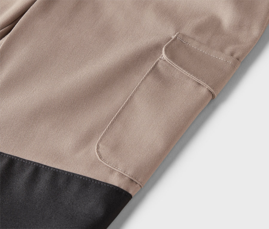 Detail béžových nohavíc s našitým vreckom a čiernou spodnou časťou.