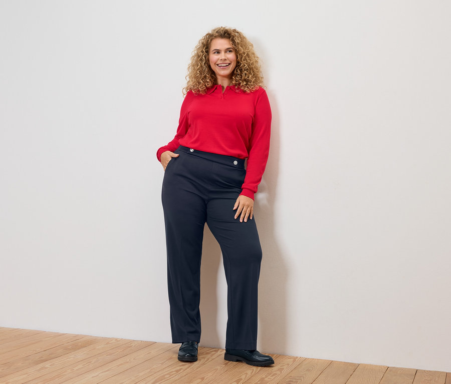 Žena s kučeravými vlasmi, v červenej blúzke a modrých nohaviciach.