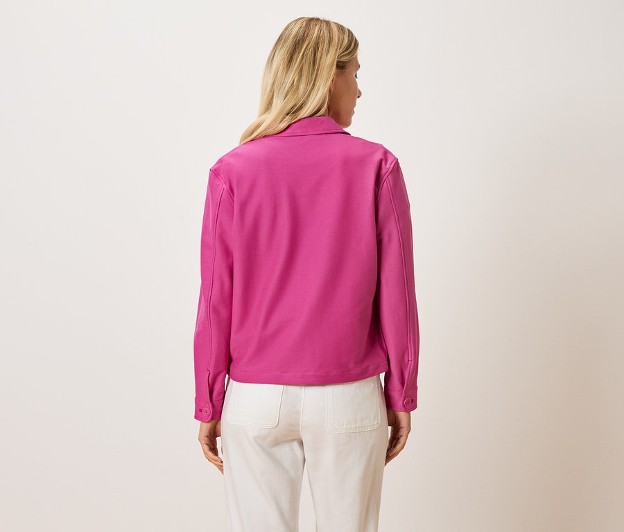 Pohľad zozadu na blondínku v ružovej bunde a svetlých nohaviciach.