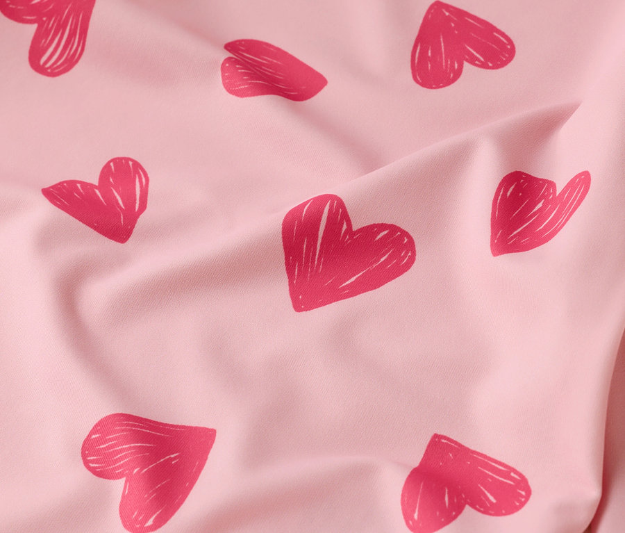 Detail záberu na pokrčenú, svetloružovú látku s červenými srdiečkami.