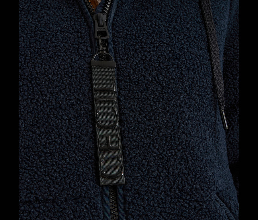 Detail tmavomodrej bundy CECIL z plyšového materiálu, so zipsom, ťaháčikom a látkovým štítkom s logom CECIL.