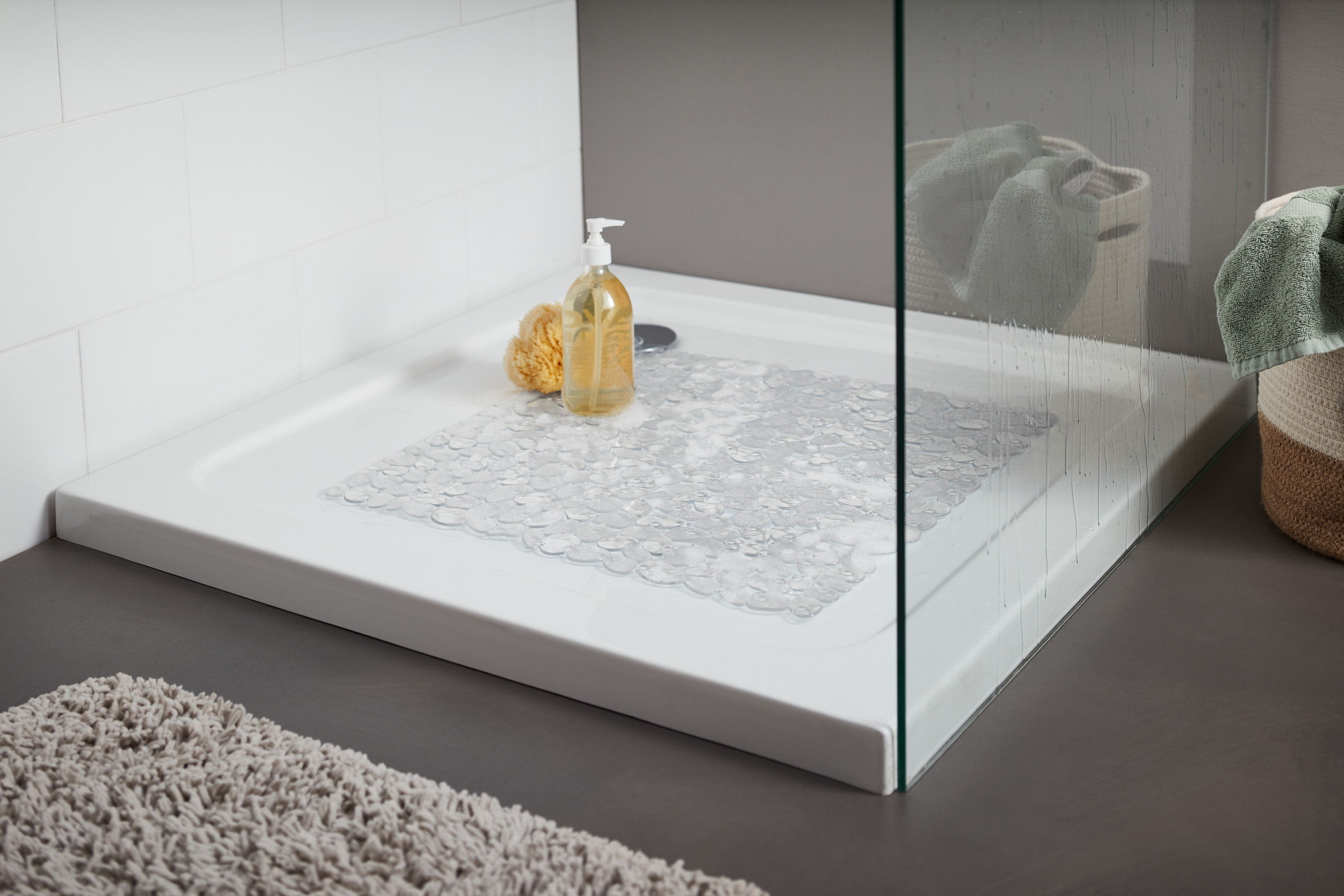 Vanička so sprchovacím kútom, v nej je položená priehľadná podložka do sprchovacieho kúta. Na vaničke je žltá umývacia huba a fľaštička s pumpičkou.