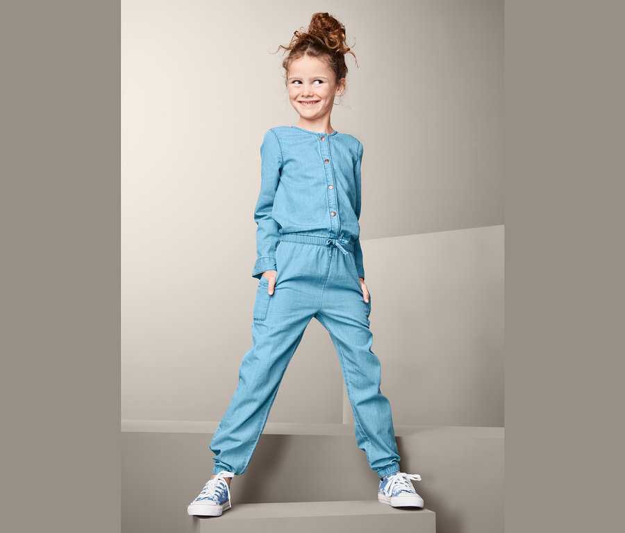 Usmievajúce sa dievča pózuje v denimovom overale.