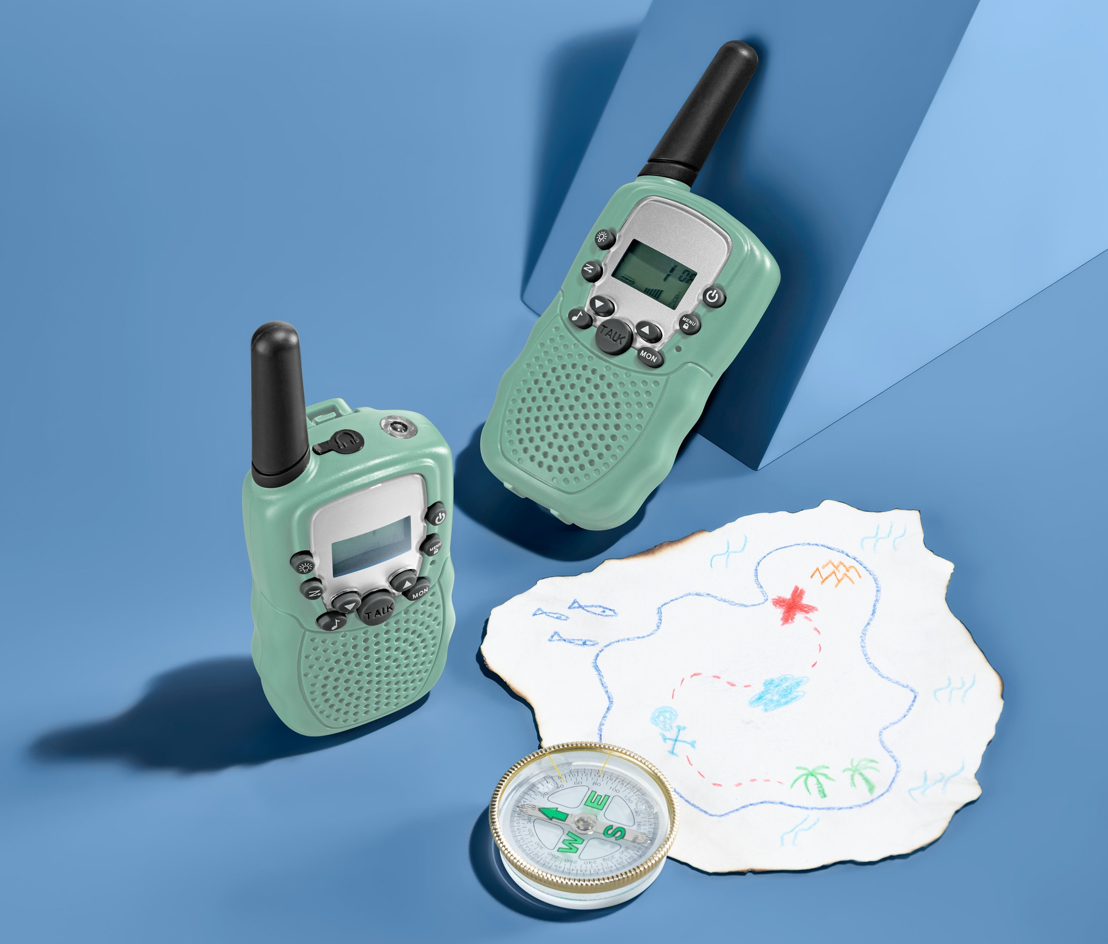 Dve detské vysielačky, kompas a mapa pokladu na modrom pozadí.