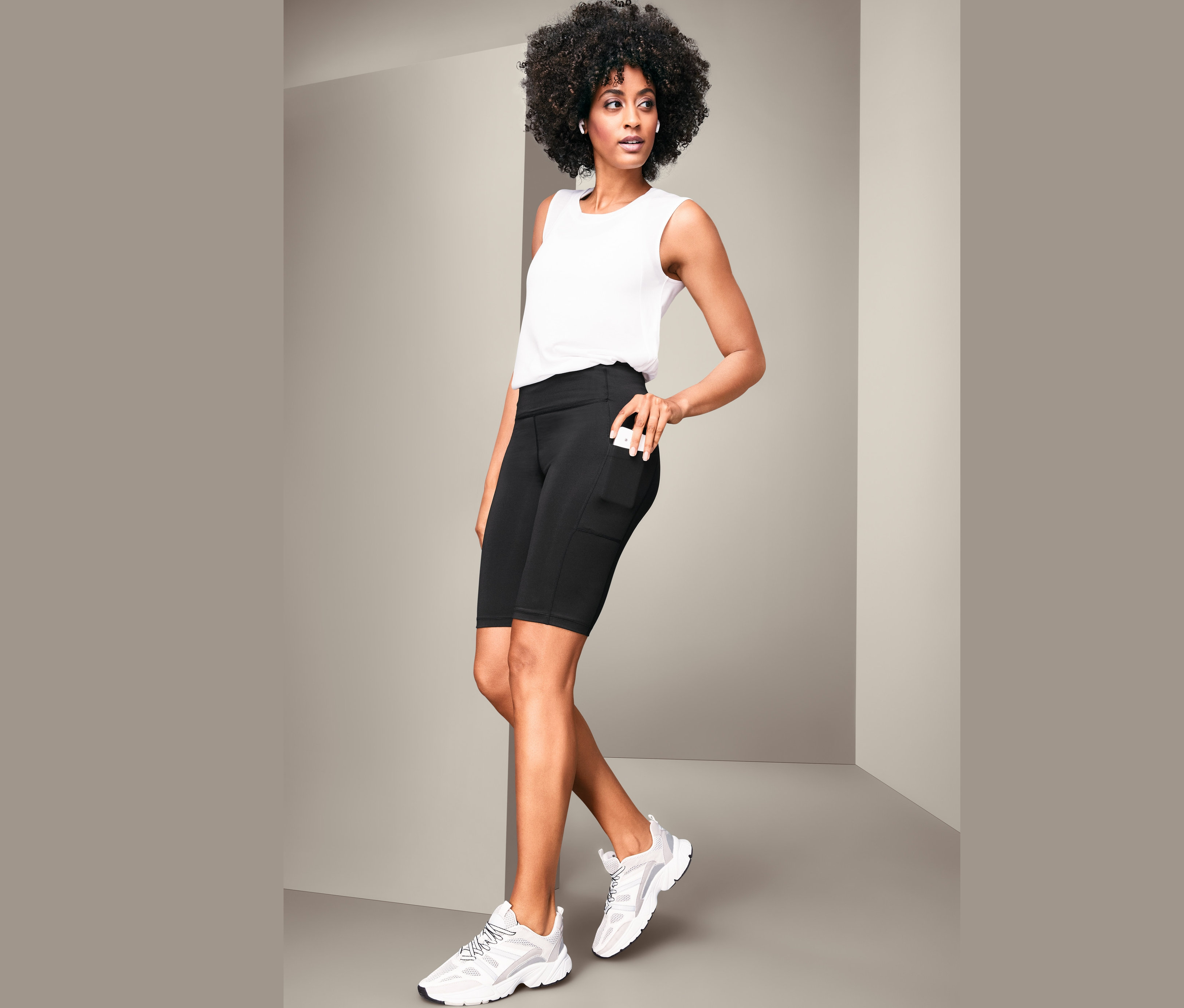 Žena pózuje v bielom tielku a čiernych cyklistických nohaviciach.