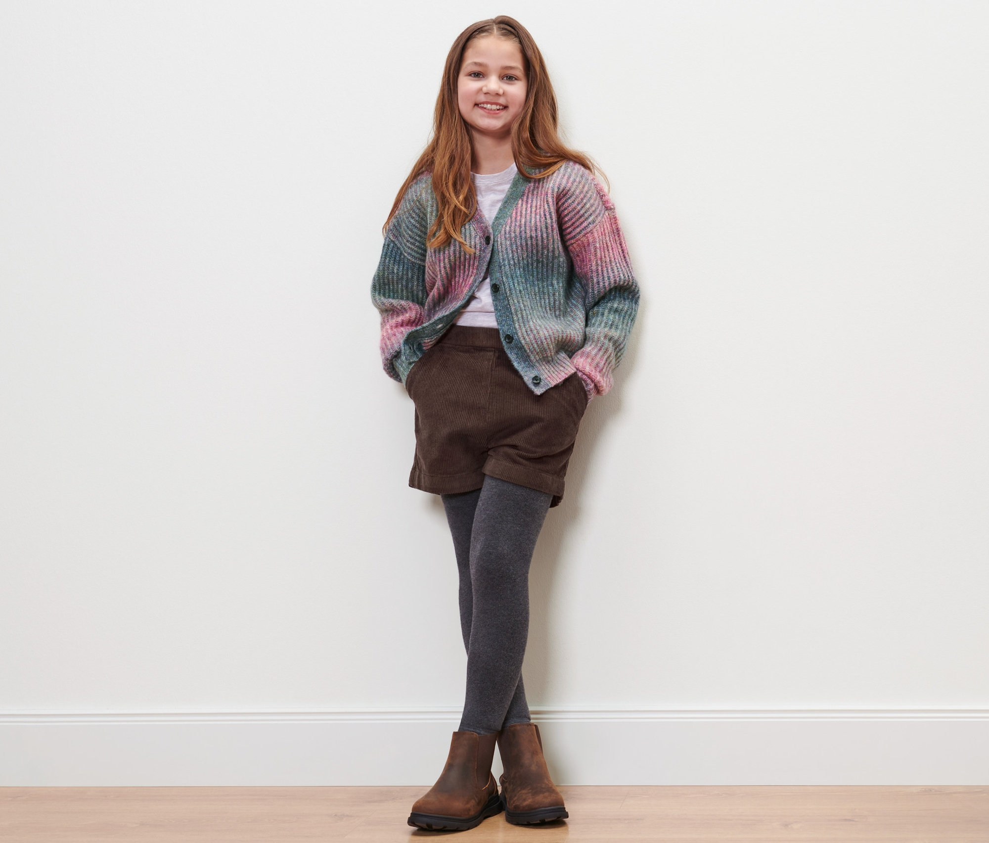 Dievča pózuje na sebe detské menčestrové šortky, sveter a topánky.