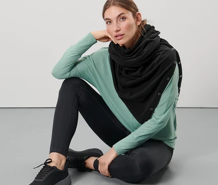 Žena sedí na zemi a má na sebe čierny šál 3 v 1 v štýle oversize.