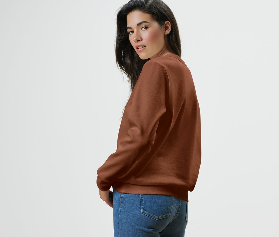 Žena sa pozerá cez plece a má na sebe mikinu a džínsy.