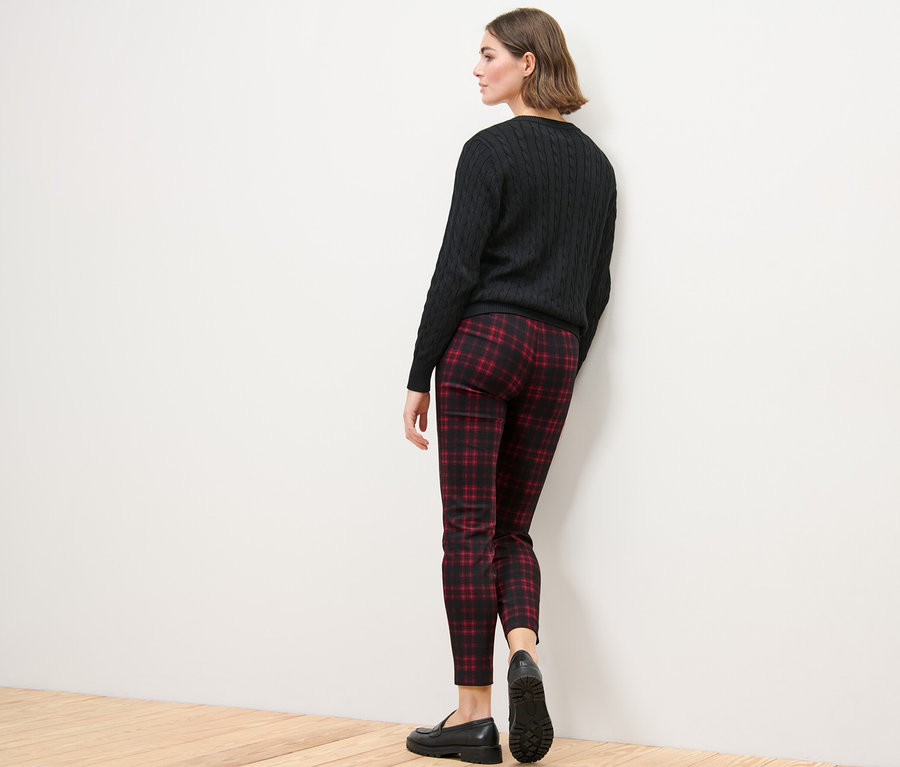 Žena stojí chrbtom k fotoaparátu a má na sebe kockované elastické nohavice, čierny sveter a čierne topánky.