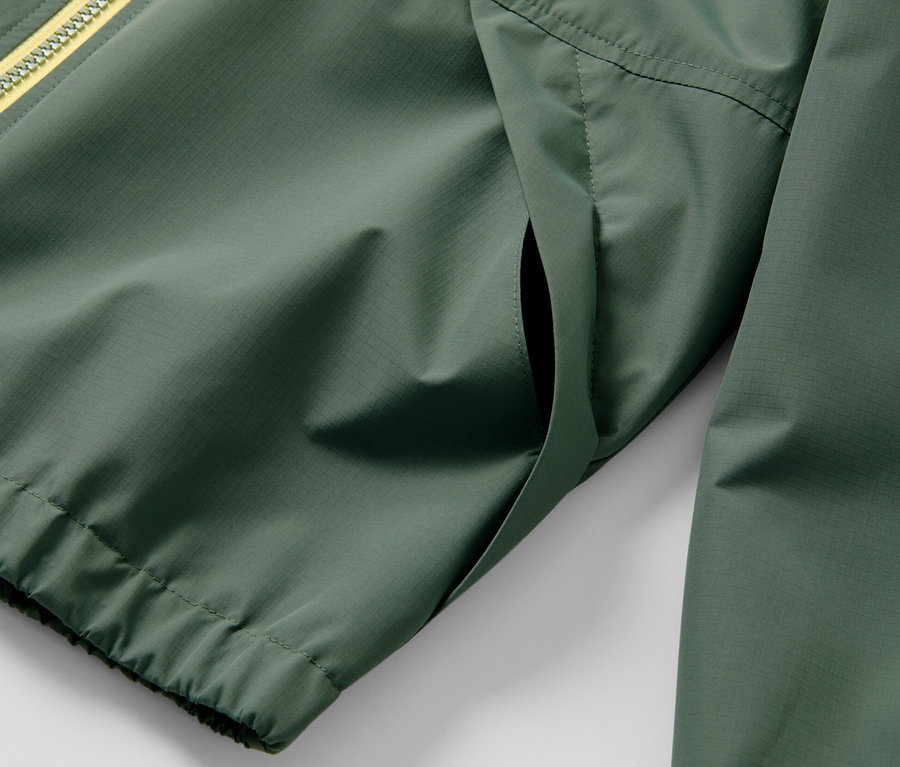 Detail zelenej detskej športovej funkčnej bundy so žltým zipsom.