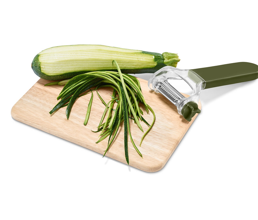 Polovica cukety, prúžky cukety a univerzálna škrabka 3 v 1 na doske na krájanie.