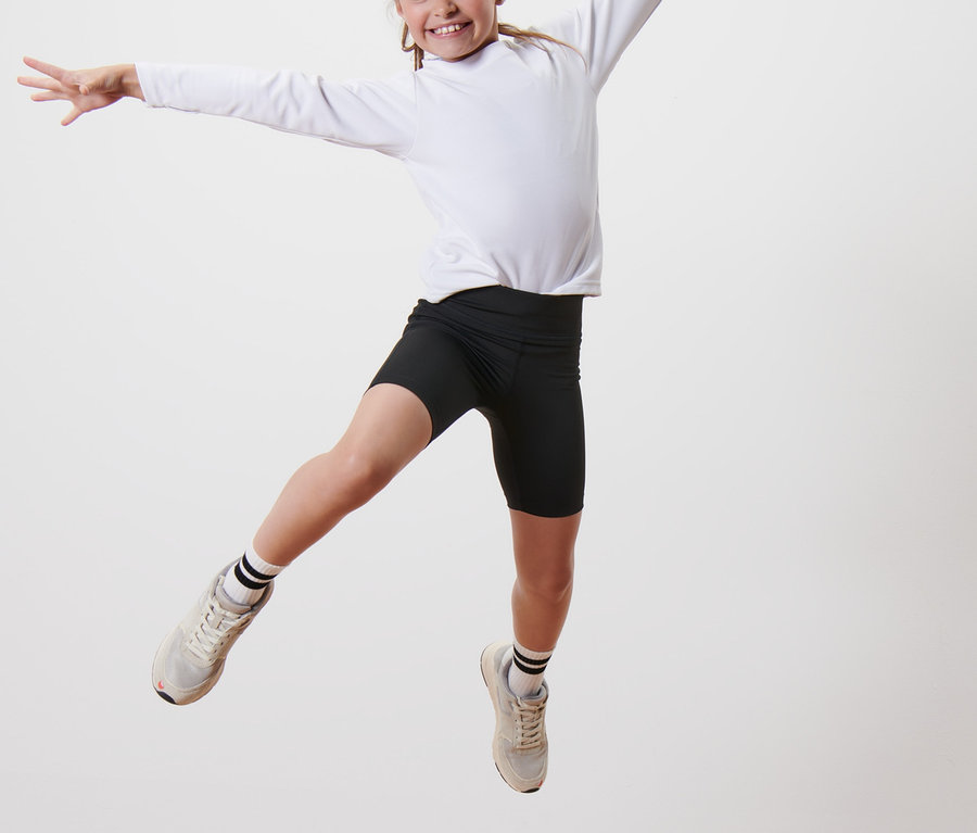 Dievča skáče na drevenom podstavci a má na sebe čierne športové šortky a biele tričko s dlhým rukávom. Na sebe má Detské cyklistické šortky, 2 ks.