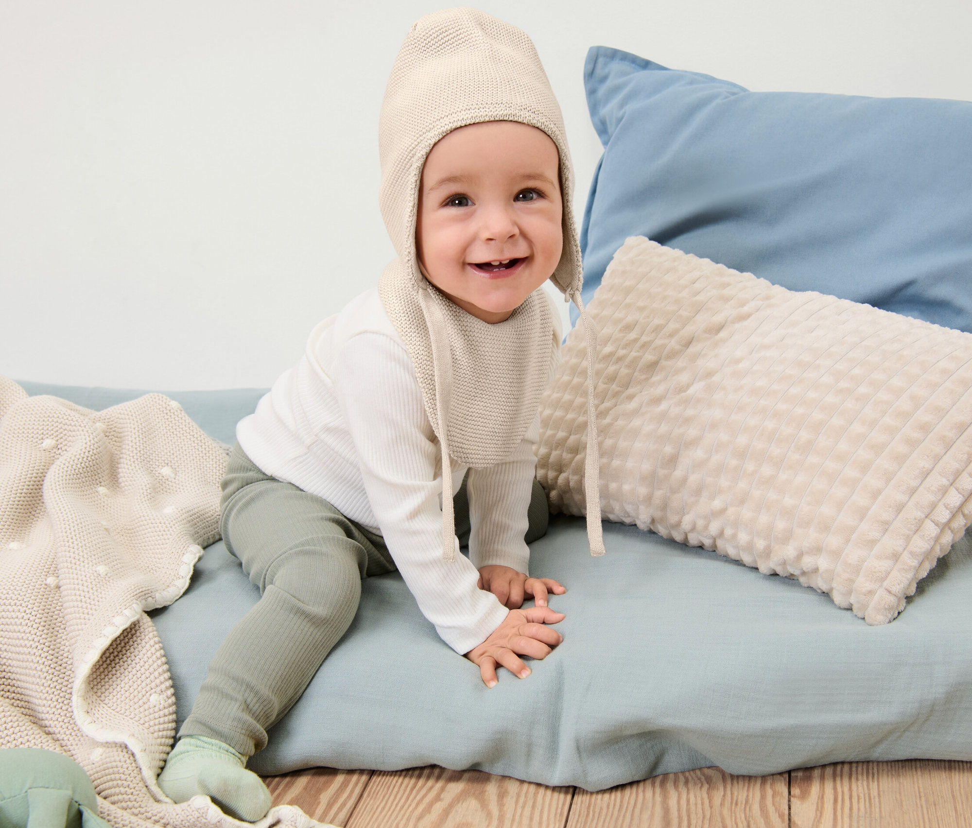 Usmievajúce sa dieťa sedí a má na sebe Detskú pletenú čiapku a pletený šál.