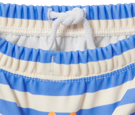 Detail detských plienok na plávanie s modro-bielymi pruhmi a oranžovou potlačou.