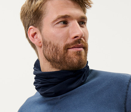 Muž s hnedými vlasmi nosí modrú multifunkčnú šatku s vlnou certifikovanou podľa RWS a modrý top.