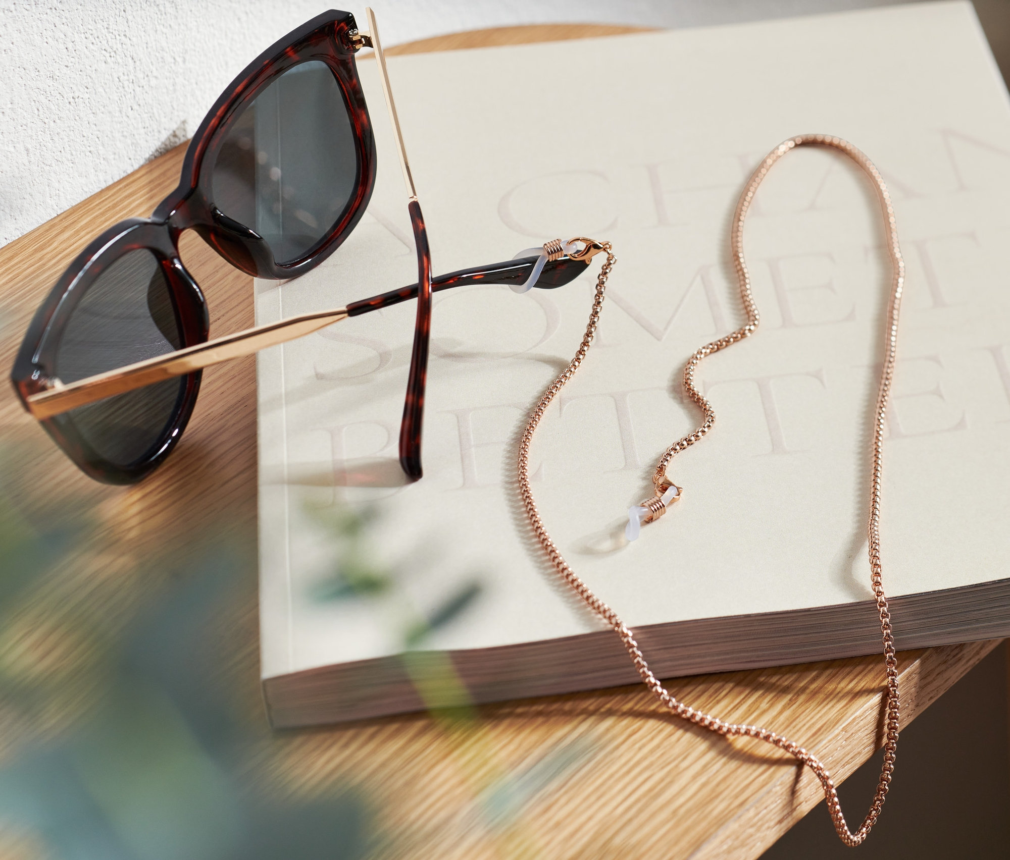 Slnečné okuliare a retiazka na okuliare ležia na knihe na drevenom stolíku.