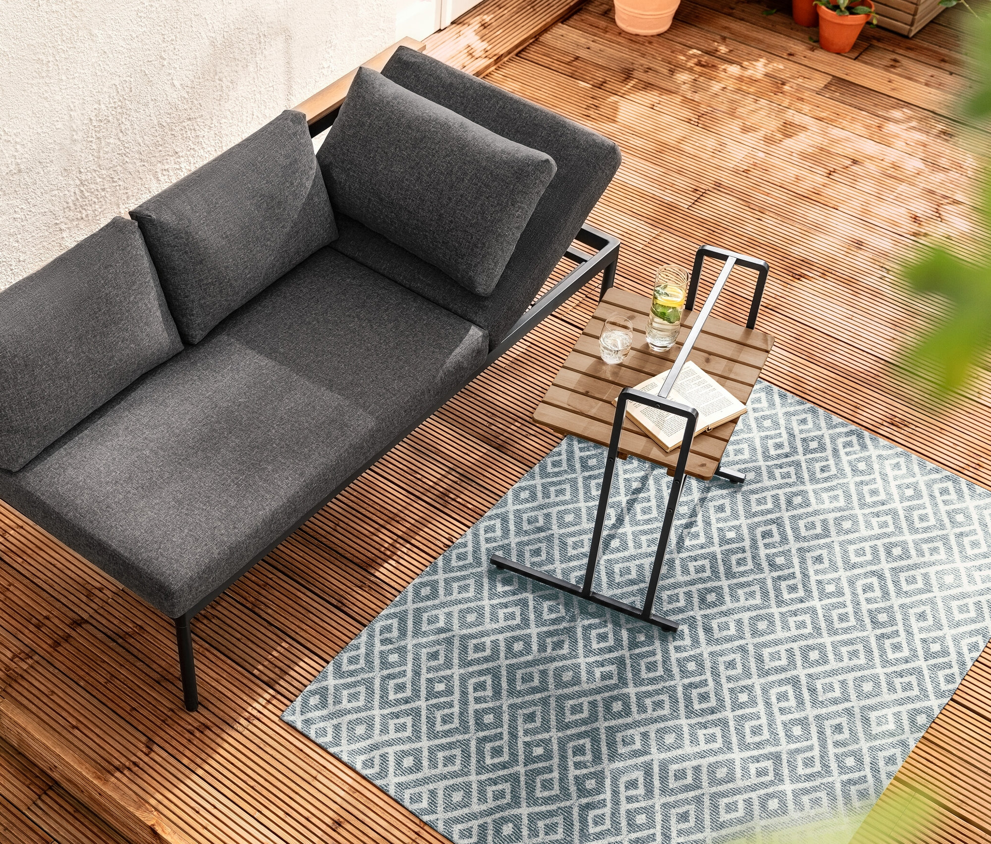 Pohľad zhora na 2 v 1 jedálenské lavicové ležadlo »Elin« vedľa C-stola s veľkou stolovou doskou na drevenej terase.