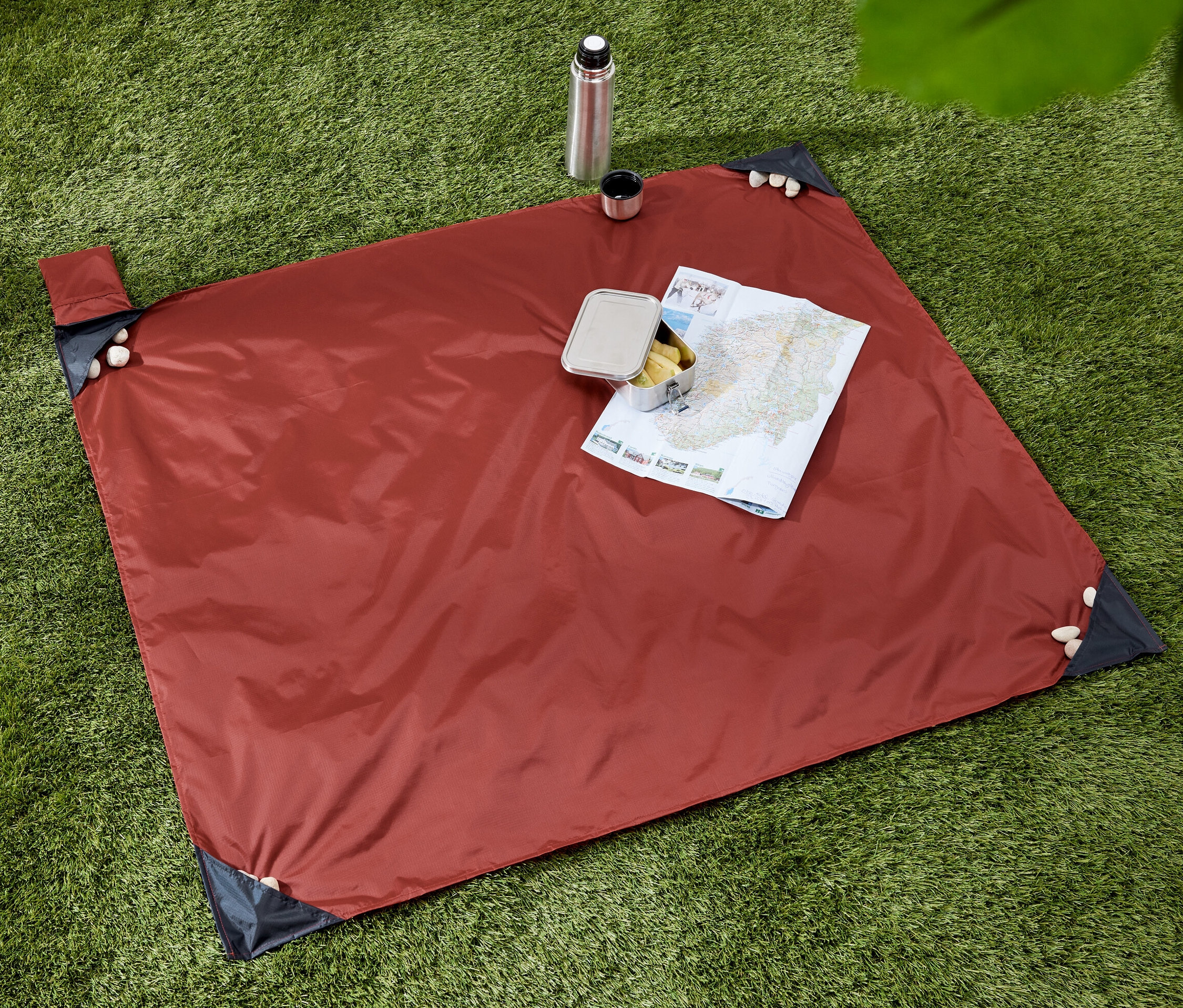 Na tráve leží malá deka na piknik, na ktorej je mapa a desiata. Vedľa deky je termoska s hrnčekom.