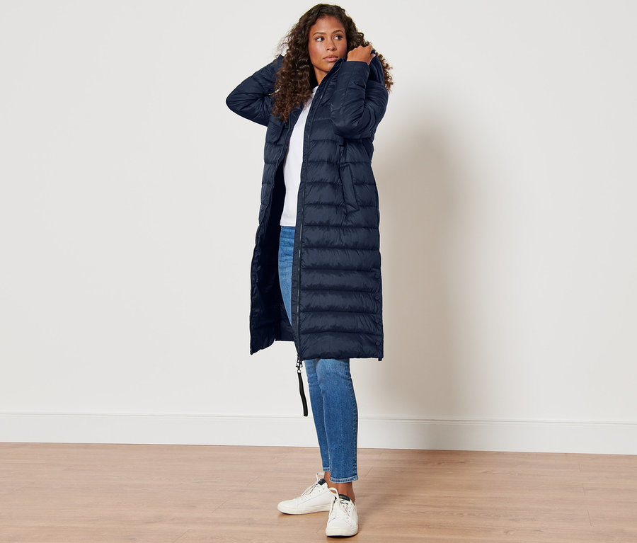 Žena pózuje v tmavomodrom prešívanom kabáte s kapucňou.