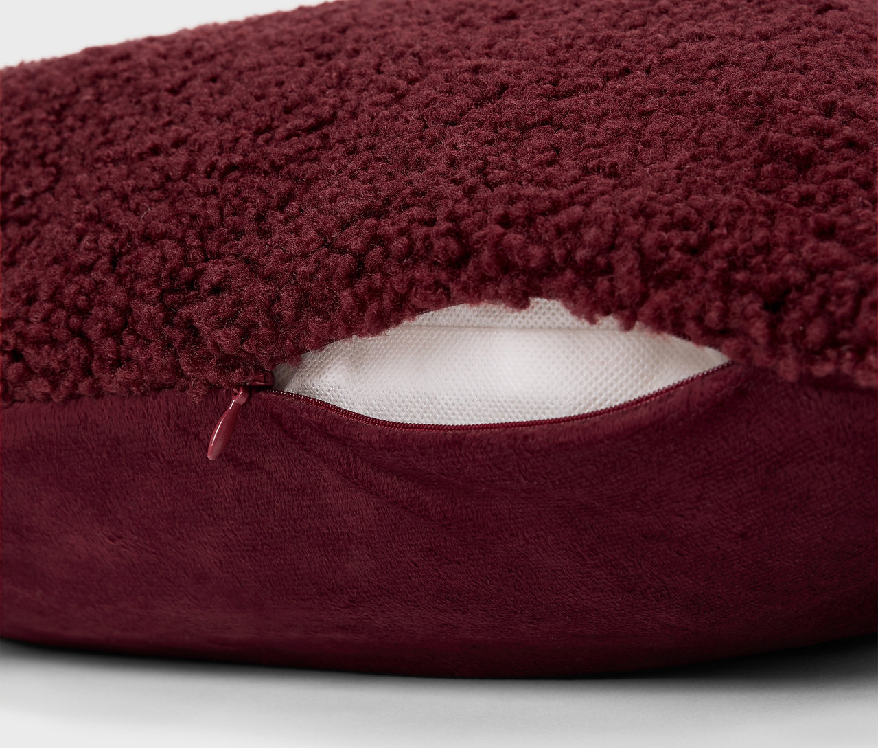 Detail bordového chlpatého vankúša so zipsom.