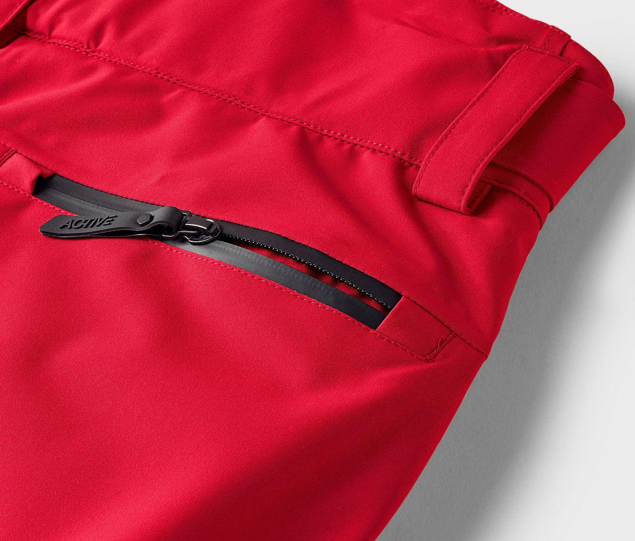 Detail červených nohavíc s čiernym zipsom na vrecku.