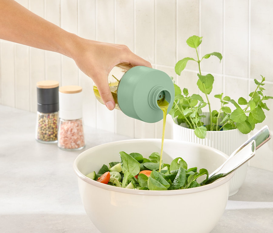 Ruka naleje dresing z fľašky na dresing do misy so šalátom.