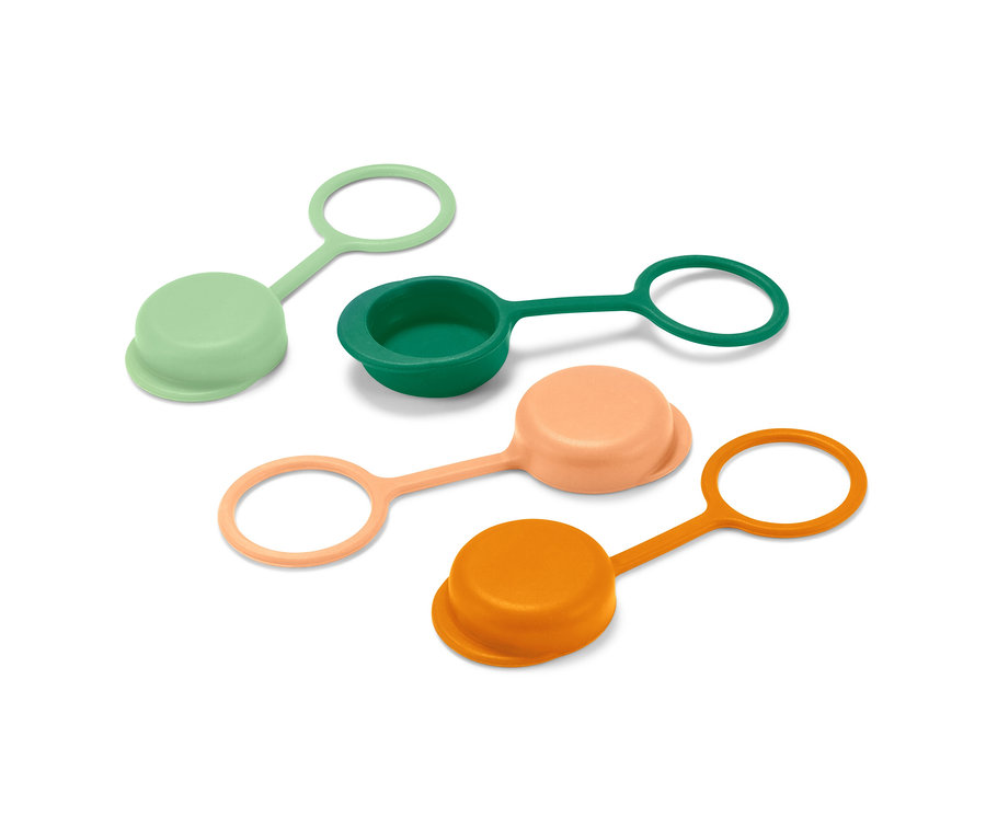 Štyri zátky na fľaše v zelenej, tmavozelenej, broskyňovej a oranžovej farbe ležia na bielom povrchu.