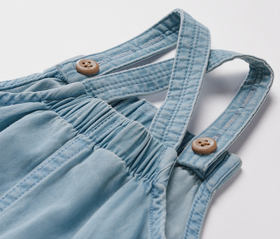 Detail detských chambray nohavíc na traky s drevenými gombíkmi.