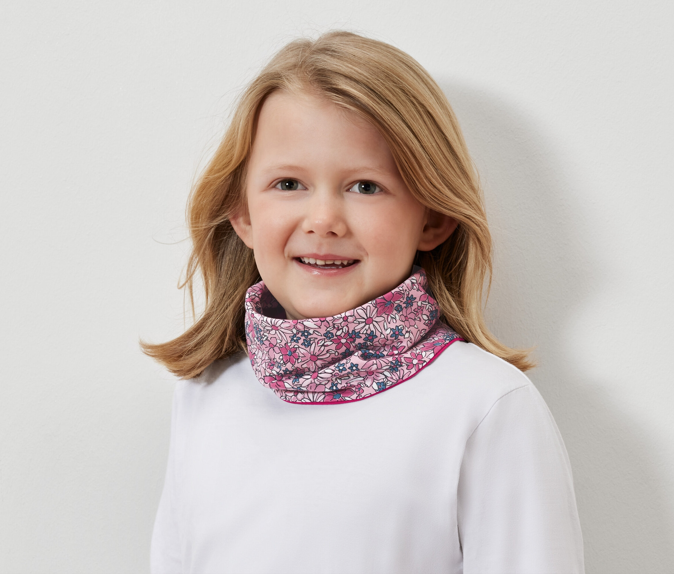 Portrét usmievajúceho sa blond dievčaťa s kvetinovým nákrčníkom.