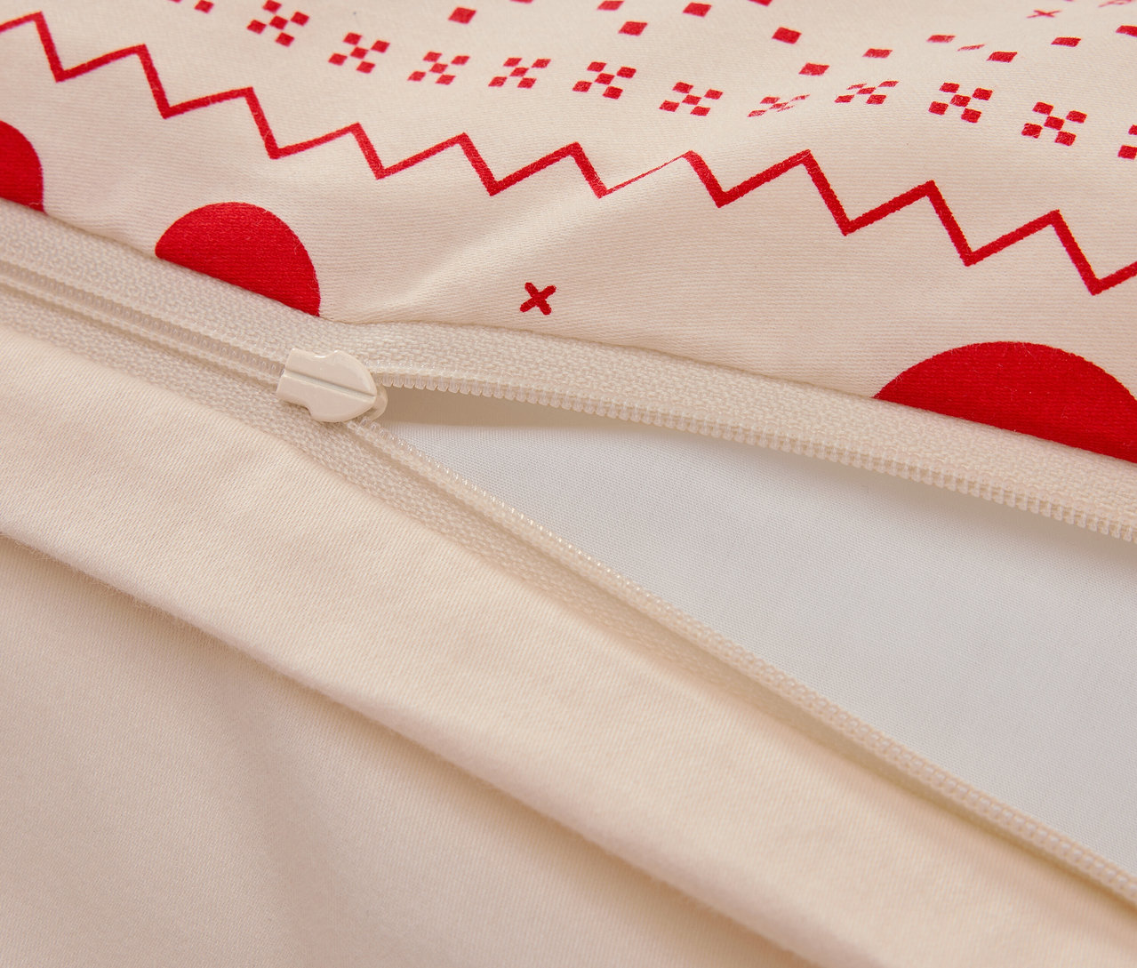 Detail bavlnenej obliečky s červeným geometrickým vzorom a zipsom.