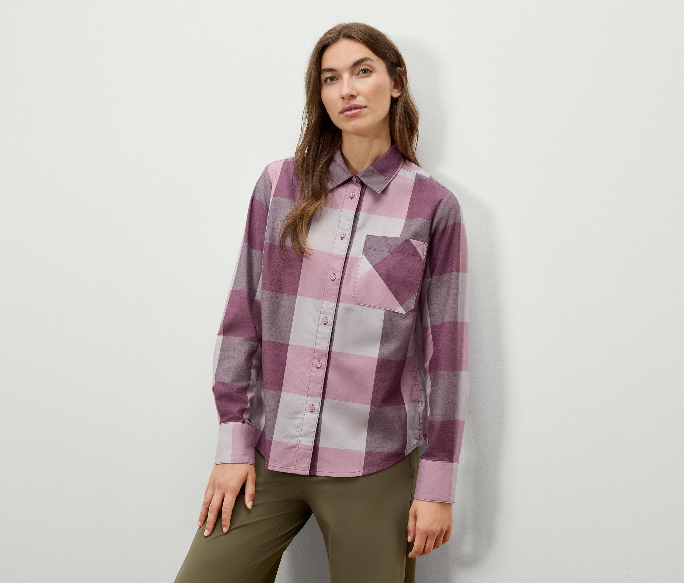 Žena pózuje v kockovanej košeli s dlhým rukávom a olivovozelených nohaviciach.