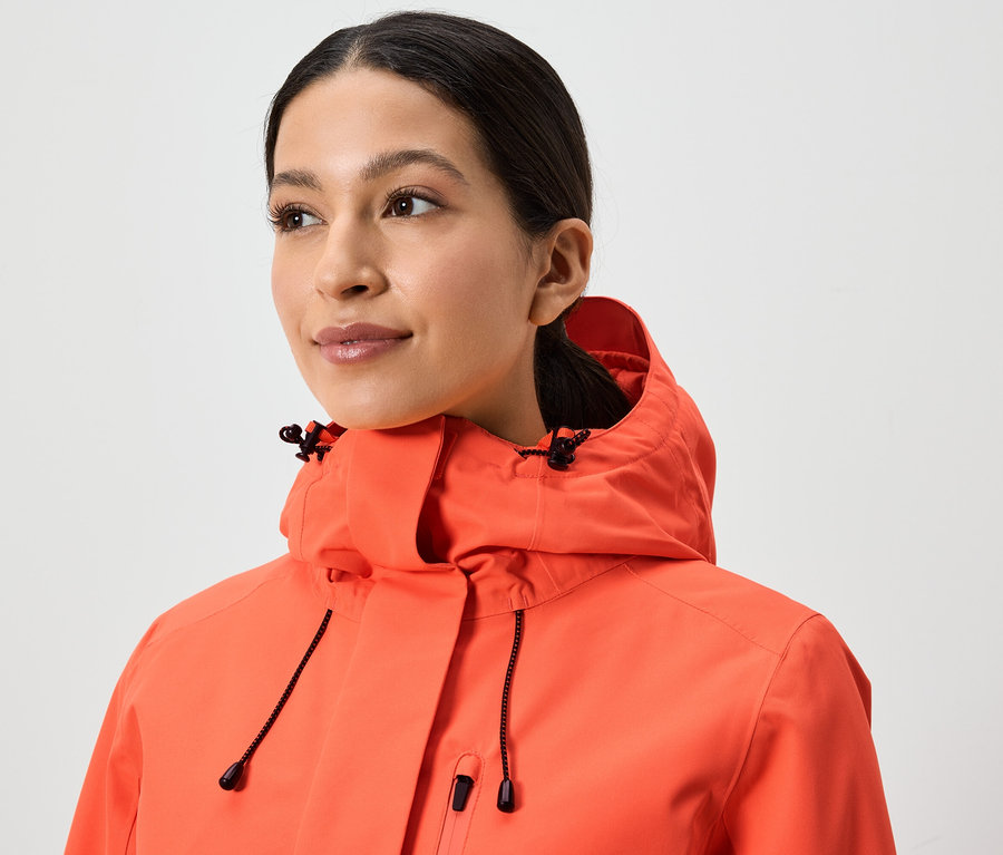 Portrét ženy v koralovej bunde s kapucňou.