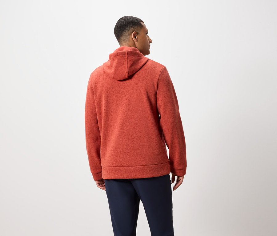 Muž chrbtom k fotoaparátu má na sebe oranžovú mikinu s kapucňou a tmavomodré nohavice.