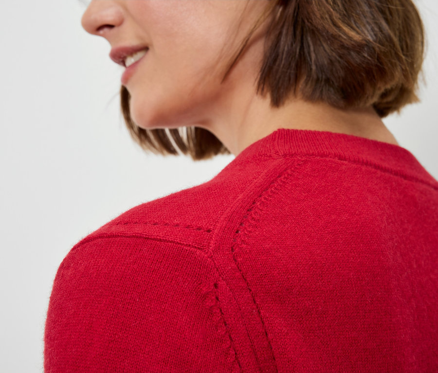 Detail dámy s krátkymi hnedými vlasmi v červenom svetri.