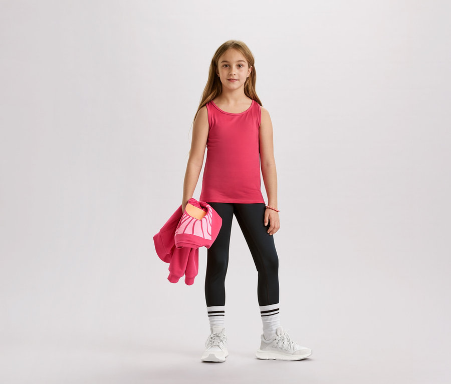 Dievča v ružovom tielku, čiernych legínach, bielych ponožkách a teniskách drží ružovú bundu a tašku.