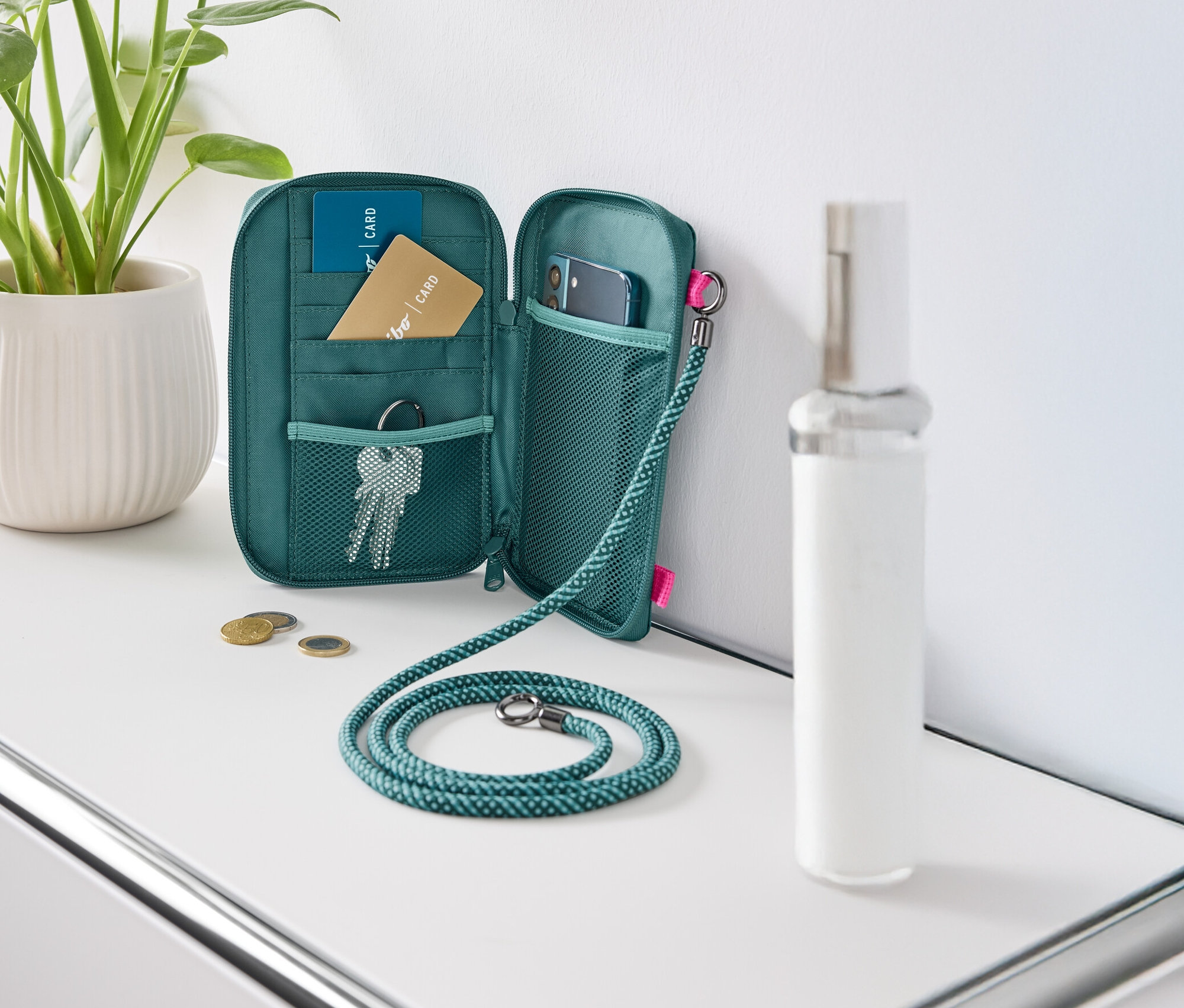 Otvorená zelená peňaženka leží na bielom stole, vyplnená kartami, kľúčmi a mobilným telefónom.