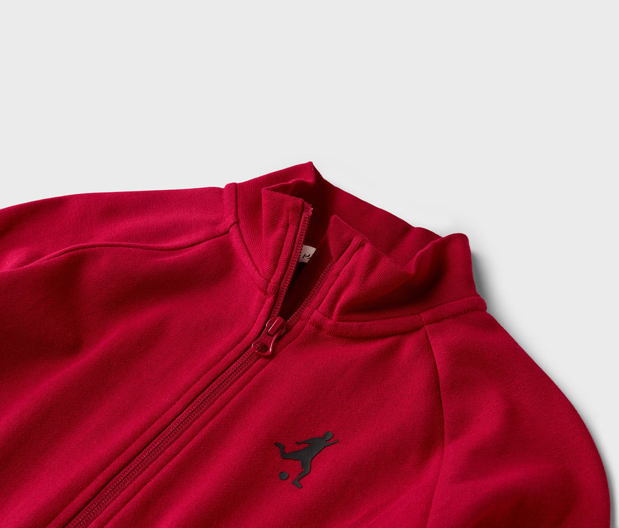 Zblízka červená tepláková bunda so zipsom a malým logom futbalistu.
