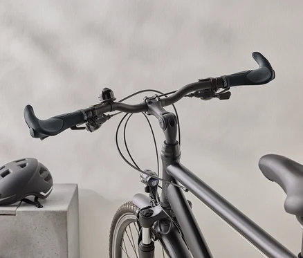 Detailný záber matného čierneho bicykla s čiernou prilbou na betónovom povrchu v pozadí.