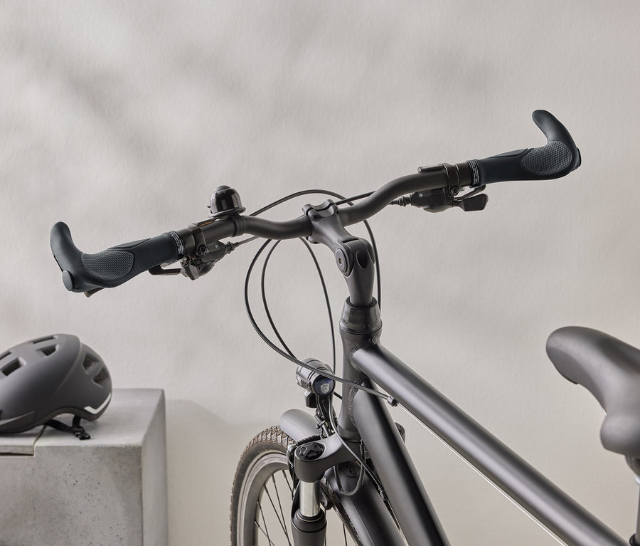 Detailný záber matného čierneho bicykla s čiernou prilbou na betónovom povrchu v pozadí.